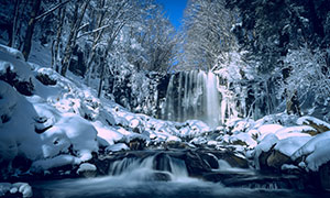 山林瀑布與覆蓋著雪的石頭攝影圖片