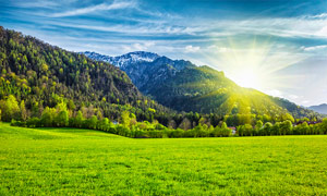 陽光下的大山和綠色草地攝影圖片